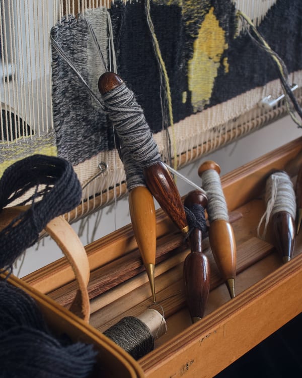 The curtain of warp is steadily worked into all manner of patterns and shades by threads with shining wooden bobbins at the end