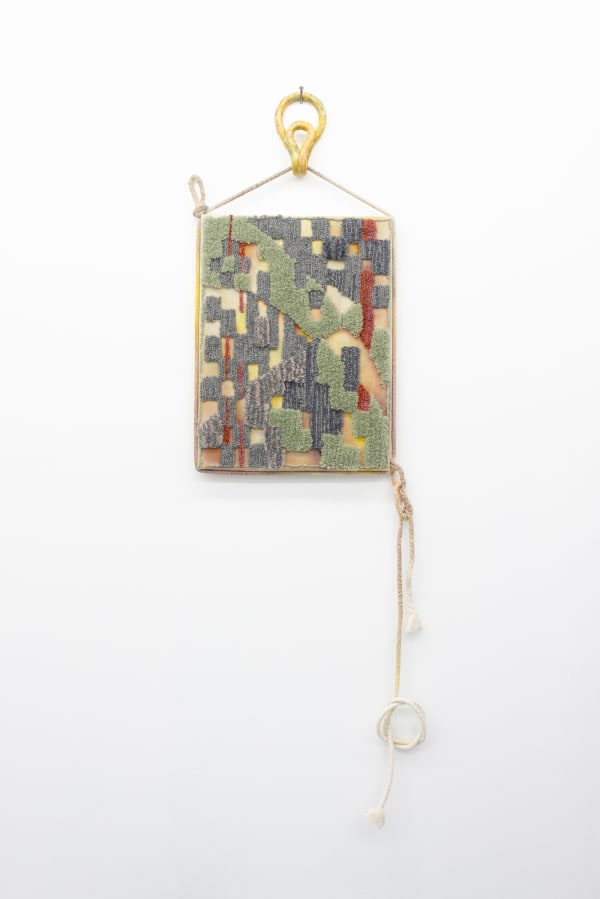Textile work with an abstract pattern. The textile is stretched and hanging on a handmade ceramic hook.