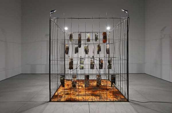 Marcin Dudek, Sektor, 2021, Steel fence, jesmonite, ash, resin, textile, medical tape, acrylic paint, image transfer, wood, uv varnish, flood lights. 240 x 210 x 210 cm - 94 1/2 x 82 5/8 x 82 5/8 in. Courtesy of Galerie Ron Mandos and Harlan Levey Projects