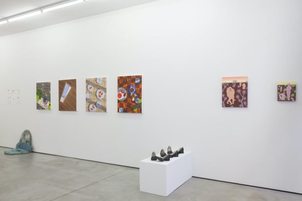 Installation view of "Buscando Recuerdos" group exhibition, pedestal with ceramic in front of gallery wall hung with various paintings 