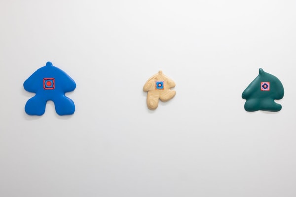 installation picture of Jocelyn Tsaih's "The Garden is Open" of three colorful wooden figures hanging on white walls