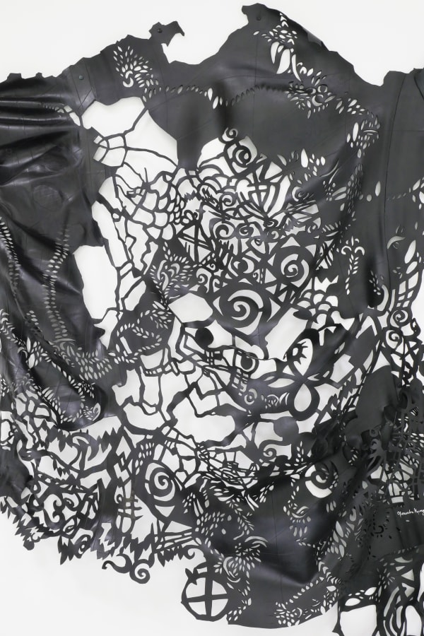 This image shows an intricate, laser-cut piece, likely made from a sheet of black material. The design is highly detailed, with interconnected patterns and motifs that create a cohesive yet complex visual tapestry. There are recognizable shapes such as sp