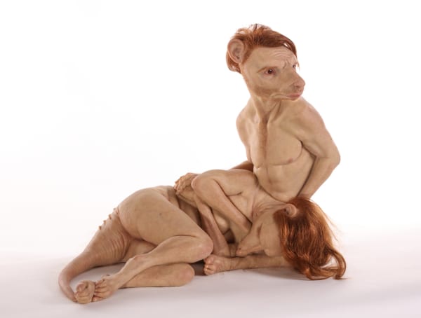 The image features a highly surreal and unconventional sculpture of a humanoid figure with distinctive, exaggerated features. The figure has an oversized head with prominent ears and an elongated, expressive face, bearing a contemplative or forlorn expres