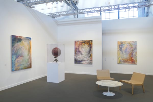 A multicolored, dabbled abstract painting is on the wall to the left, the perpendicular wall and another behind it have similar paintings. A red globe sits in a case in between the first two paintings. to the right of the globe and closer in the foregroun