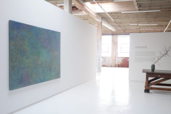 I picture of an art gallery with white walls and a blue panting hung on the wall