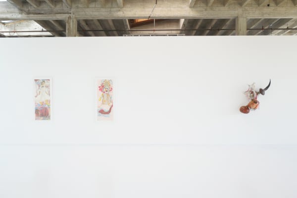 The image shows a contemporary art gallery installation featuring three framed artworks and a sculptural piece displayed on pristine white walls. The artworks on the left wall appear to be colorful and abstract, while the piece on the right wall includes