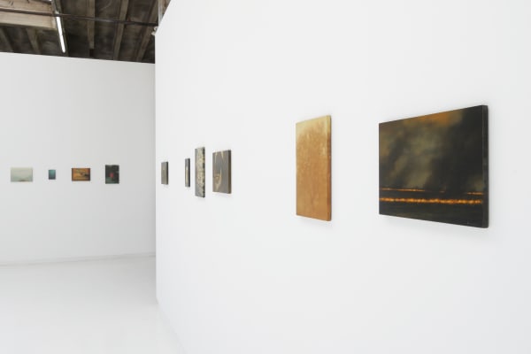 side angle view of wall with 6 small paintings hung horizontally next to perpendicular wall with four small paintings also hung horizontally
