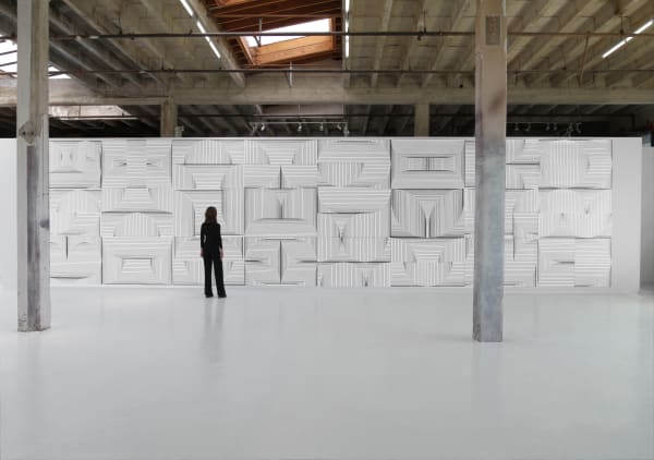 Woman in all black stands in gallery with walls covered in linear ink drawings by Tim Hawkinson.