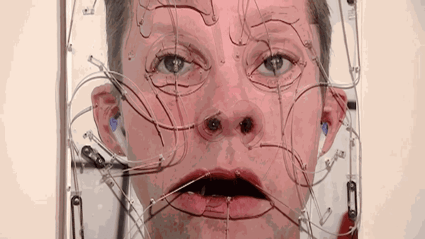 Photograph of white man's face with glass overlaid with various strings looking as though they are pulling pieces of the face in different directions.