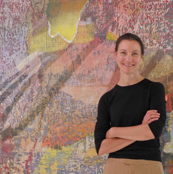 The artist standing in front of her painting smiling with arms crossed. The painting is pink and abstract.
