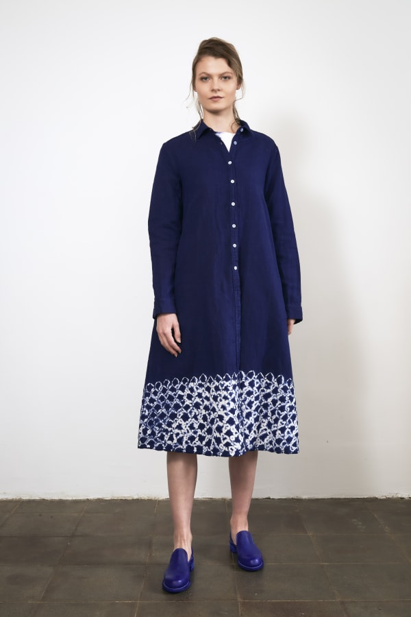 A woman in a blue button down triangular dress, with white details on the bottom that look like scalloping.