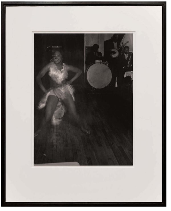woman in white fringe outfit dancing with jazz musicians in background from Paris de Nuit by Brassai