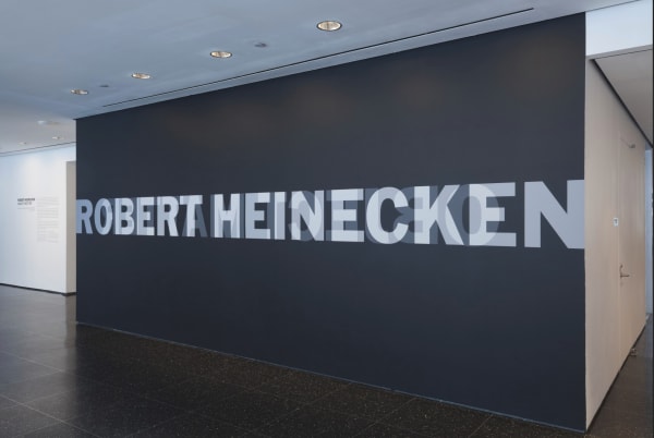 Robert Heinecken exhibition entrance at the Museum of Modern Art, with the artist's name in capital letters in white on a black wall overlaid in the style of the para-photographer