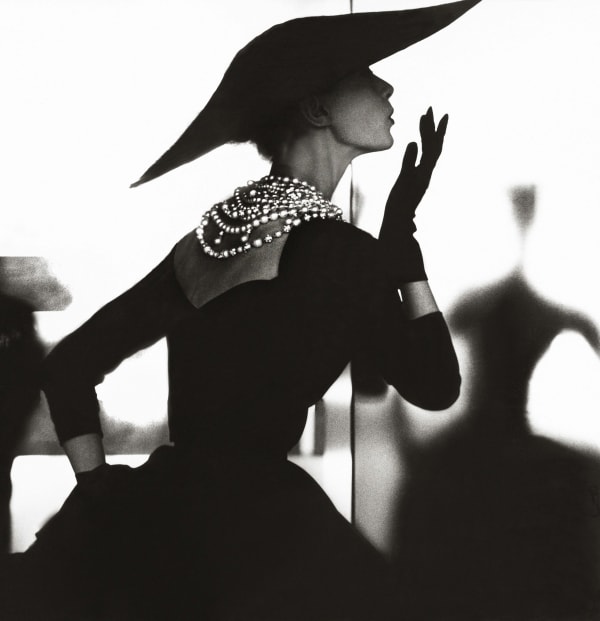 Fashionable woman wearing hat, gloves and pearls blowing a kiss, by Lillian Bassman