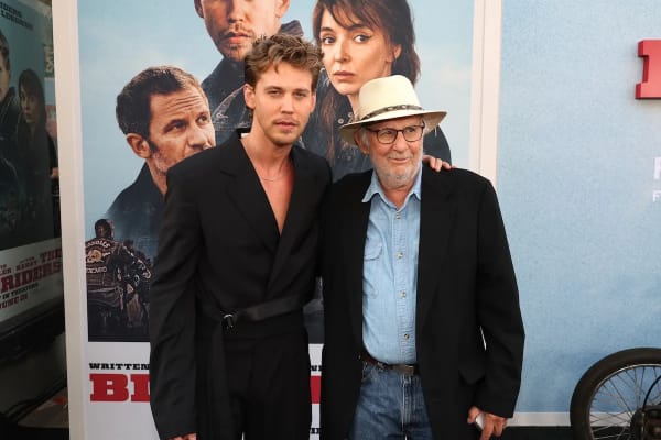 Austin Butler and Danny Lyon pose in front of The Bikeriders movie poster
