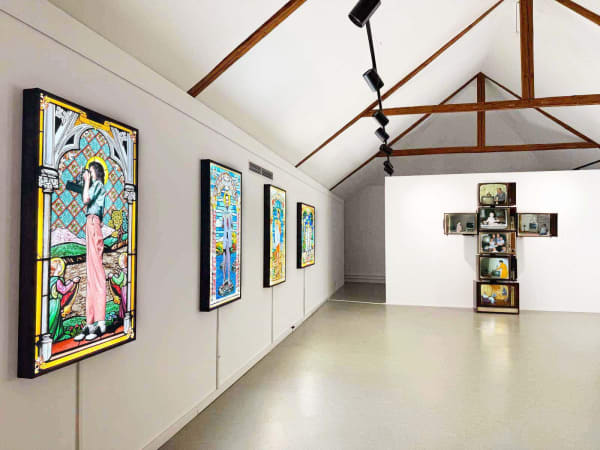 installation shot inside a castle of stained glass and a tv video installation shaped like a cross
