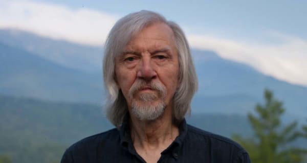 Color portrait of Arno Rafael Minkkinen against a mountainous backdrop.