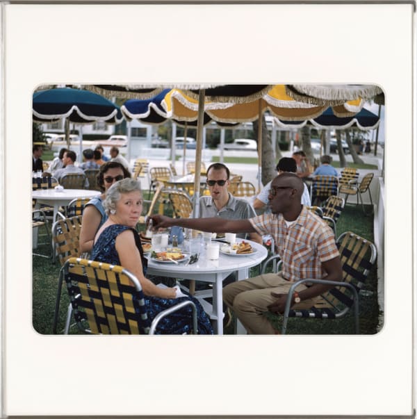 Omar Victor Diop appears in a vintage scene, seated at an outdoor café table.