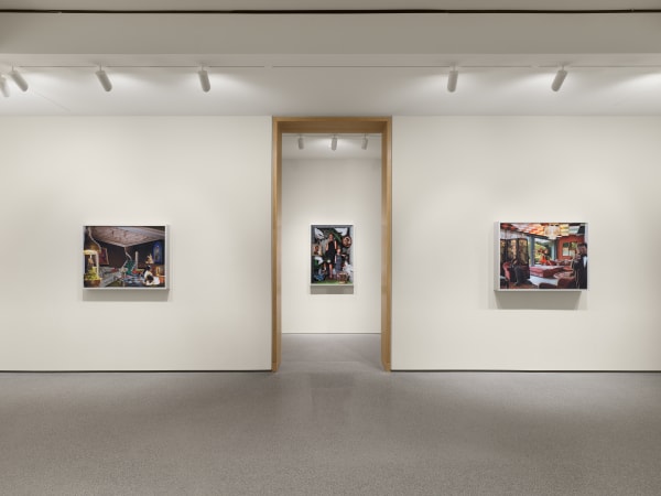 Three framed photographs hang on a white gallery wall, symmetrically arranged around a doorway, under track lighting in a minimalist exhibition space.