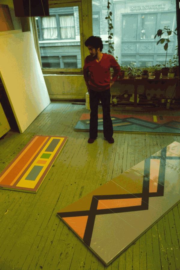 Freddy Rodríguez standing alongside paintings Danza de Carnaval (1974), Amor Africano (1974), and Untitled (1970)