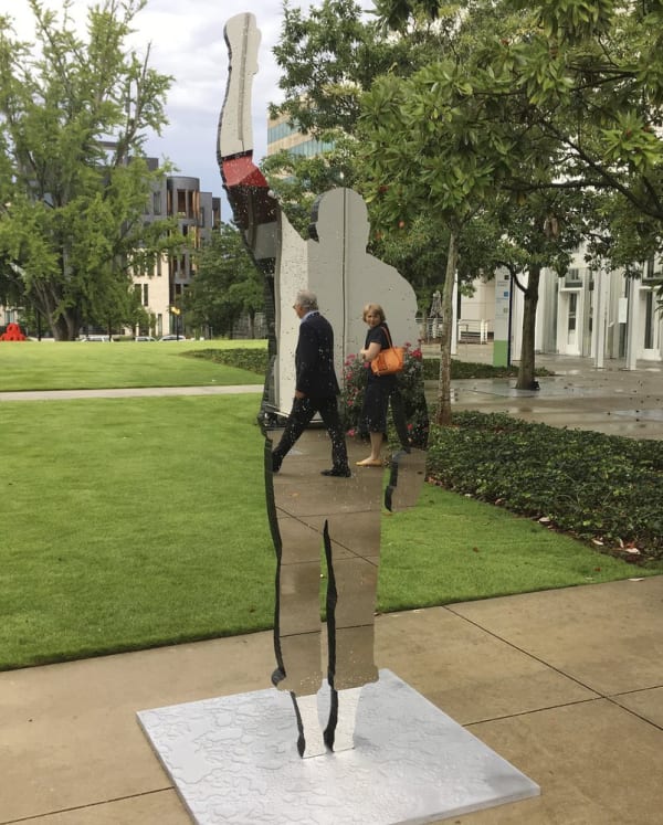 In this Sept. 26, 2018, photo, people can be seen reflected in the mirrored surface of a sculpture outside the High Museum of Art in Atlanta. The sculpture "Invisible Man (Salute)" is part of an exhibition titled "With Drawn Arms: Glenn Kaino and Tommie Smith," which reflects on a protest by African-American sprinters at the 1968 Summer Olympics. The front of the sculpture is a flat, mirrored surface, while the back is a lifelike statue of Olympian Tommie smith on the medal podium with his arm raised in protest. (AP Photo/Kate Brumback)