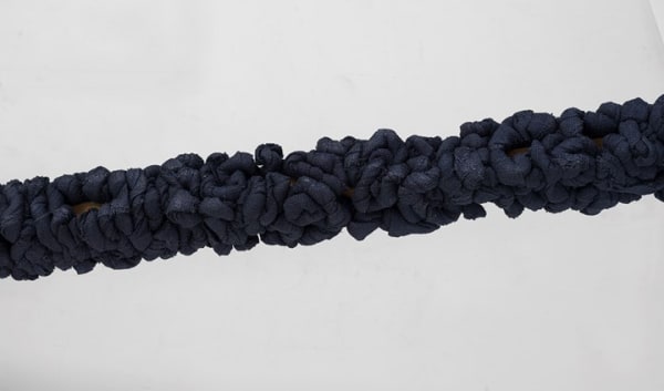 Manish Nai’s Untitled (2017): five large sticks wrapped in compressed strips of burlap dyed indigo leaning upright against a wall.
