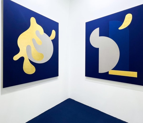Image of exhibition with two of Sinta Tantra's works defined by their vibrant blue background and gold and grey overlapping shapes.