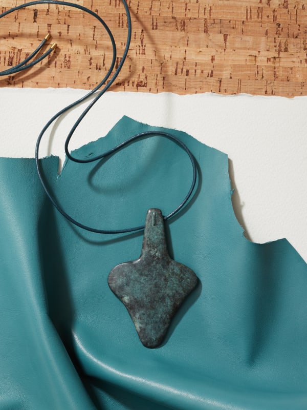 William Turnbull, Metamorphosis Pendant, 2012, bronze, 22k gold suspensory loop on reverse, leather cord with 18k gold fixings on limestone & bronze stand. Inscribed with the artist's stamp, numbered & hallmarked. 9.7 × 6.2 × 0.5 cm. 95 g. Edition of 25 + 8 AP in collaboration with Louisa Guinness.