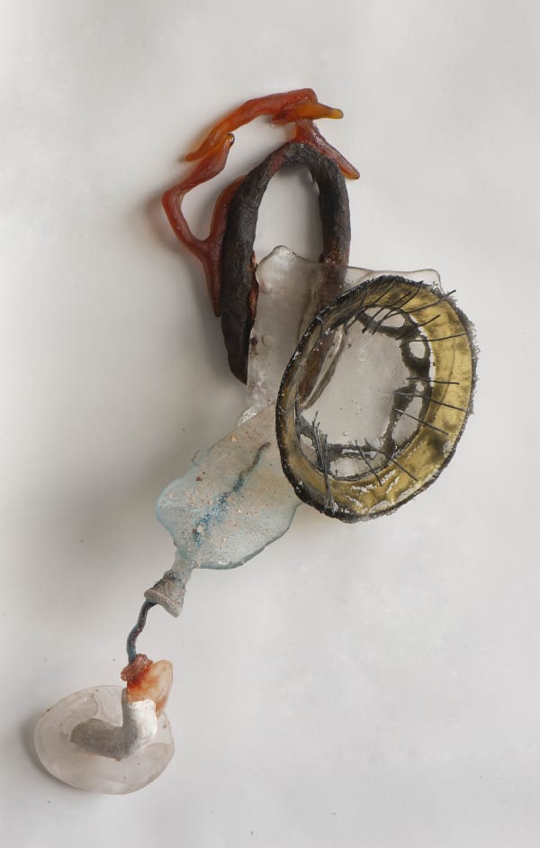 Nancy Cohen's "Issue" art piece made out of glass, metal and ceramic. The medium used are colored in shades of yellow, orange, blue, clear, brown and black. Pieces of glass are layered on top of each other attached to a metal wire on a small clear stand.