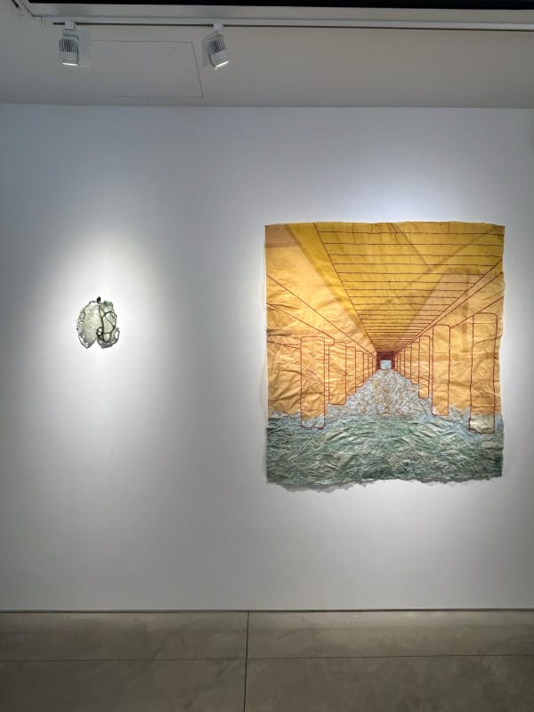 photo of an installation with one large work on paper hanging to the right of a small sculpture on the wall.
