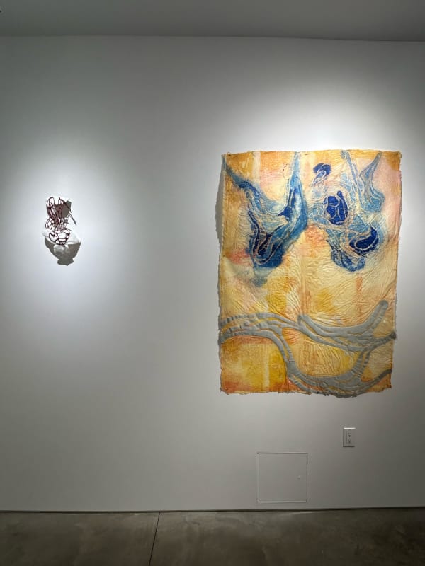 photo of an installation with one large orange price of art on paper, and one small sculpture hanging to the left of it.
