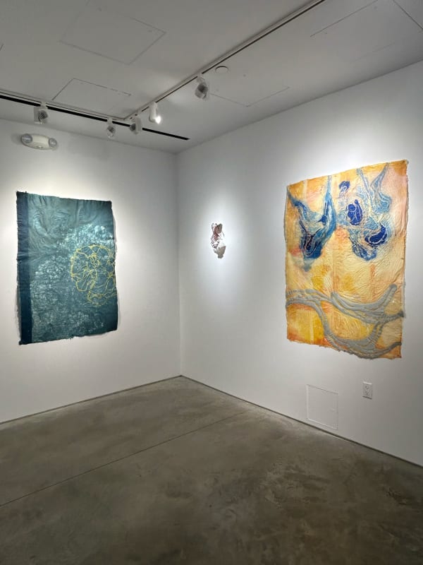 photo of an installation with two large works, and one small sculpture between them. the leftmost work is blue, and the rightmost is primarily orange.