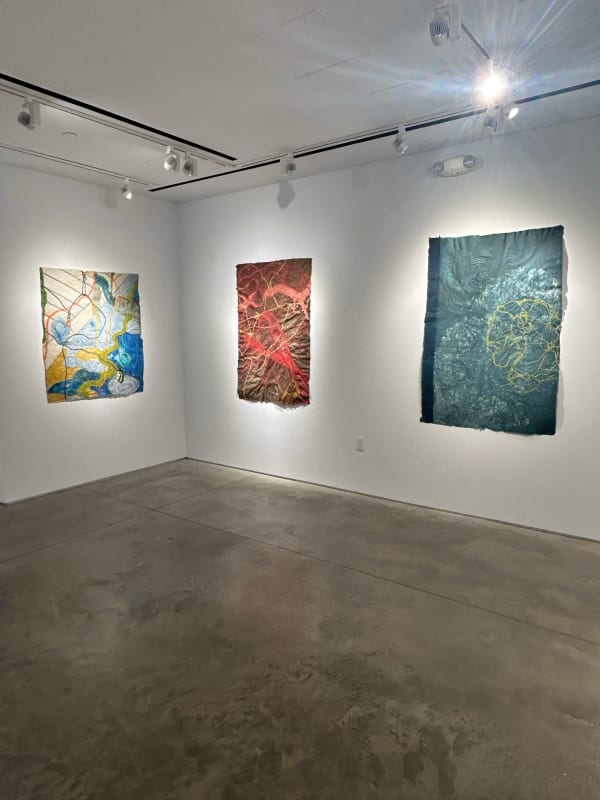 photo of an installation with three large works on paper on the walls. From left to right, they are mostly white, red, and blue