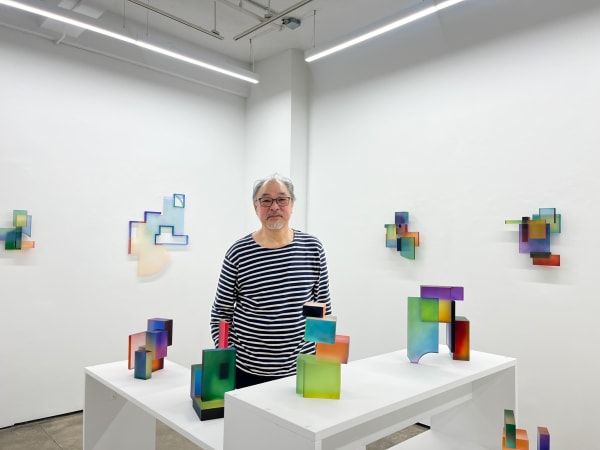 Greg Chan Standing in a gallery full of his sculptures.
