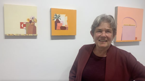 Woman standing in front of three small still life paintings on a gallery wall.
