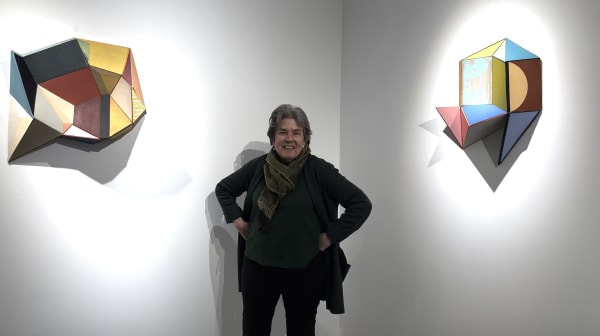 Woman standing between two gallery walls with colorful geometric collage sculptures on each side of her.