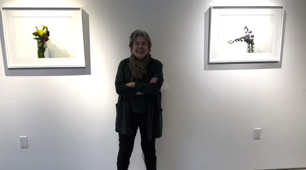 Woman standing between two small abstract floral paintings hanging on a gallery wall.