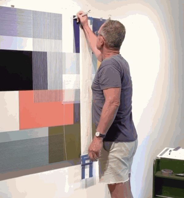 Man drawing lines on an abstract painting hanging on a studio wall