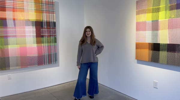 Woman standing in a gallery between two colorful abstract geometric paintings on the gallery walls.