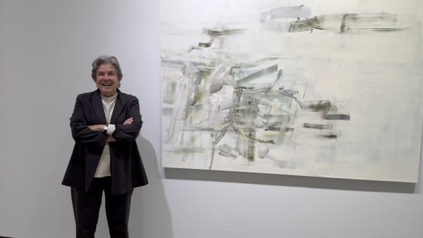 Woman standing in front of a large abstract painting in muted colors hanging on an art gallery wall
