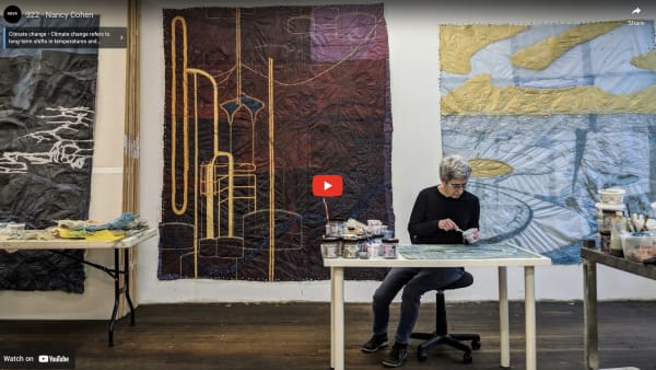 Female artist at table with large paper drawings in the studio behind her