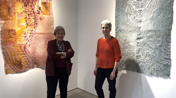 Two women standing in front of two large, colorful paper drawings in an art gallery.