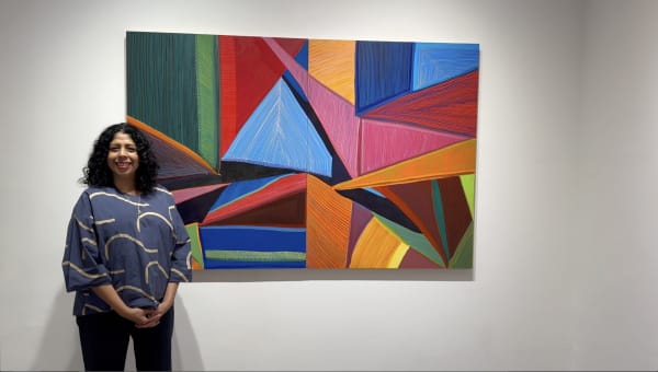 Dark-haired woman standing in front of colorful, abstract geometric painting, hanging on an art gallery wall.