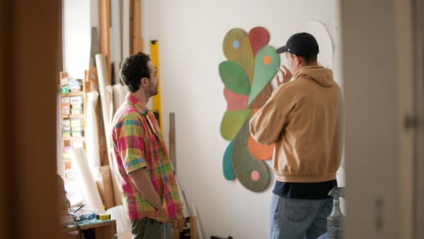 Two men standing in front of painting in an artist studio.