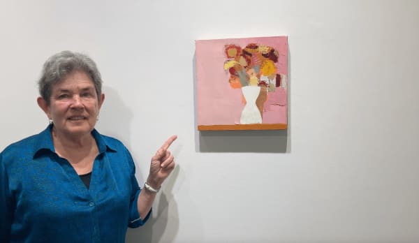 Kathryn Markel pointing to a floral painting by Sydney Licht.