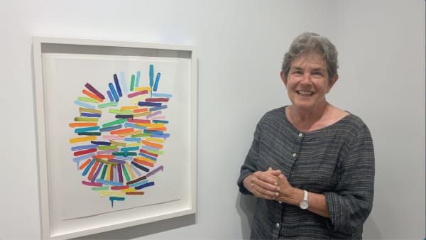 Woman standing next to a framed painting of multi- colored brushstrokes.