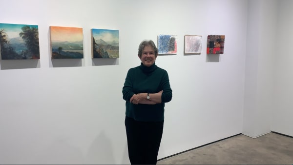 Woman standing in front of six small artworks.