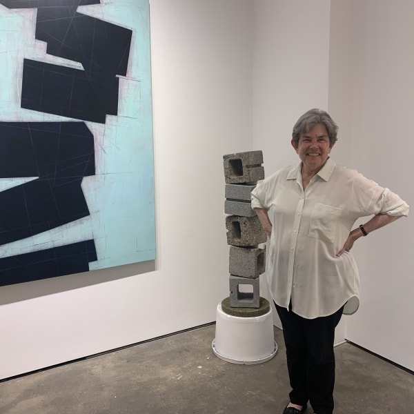 Woman standing in art gallery in front of cinderblock sculpture and blue abstract painting.
