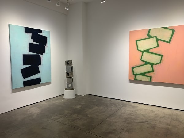 Two abstract paintings and a concrete block sculpture in a gallery.