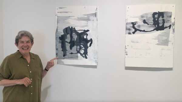 Woman pointing at two black and white, abstract paintings on paper.